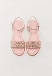 Light pink sandals with studded straps, adjustable ankle strap, flat sole, smooth texture, and minimalistic design.
