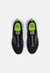 Pair of black and grey athletic shoes with white speckled soles and neon green insoles featuring a circular flower-like logo, viewed from above.