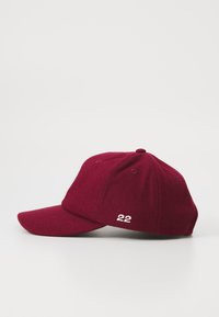 Casquette de baseball couleur bordeaux, en tissu texturé, avec un visière incurvée et le numéro brodé "22" à l'avant. Six trous de ventilation visibles.