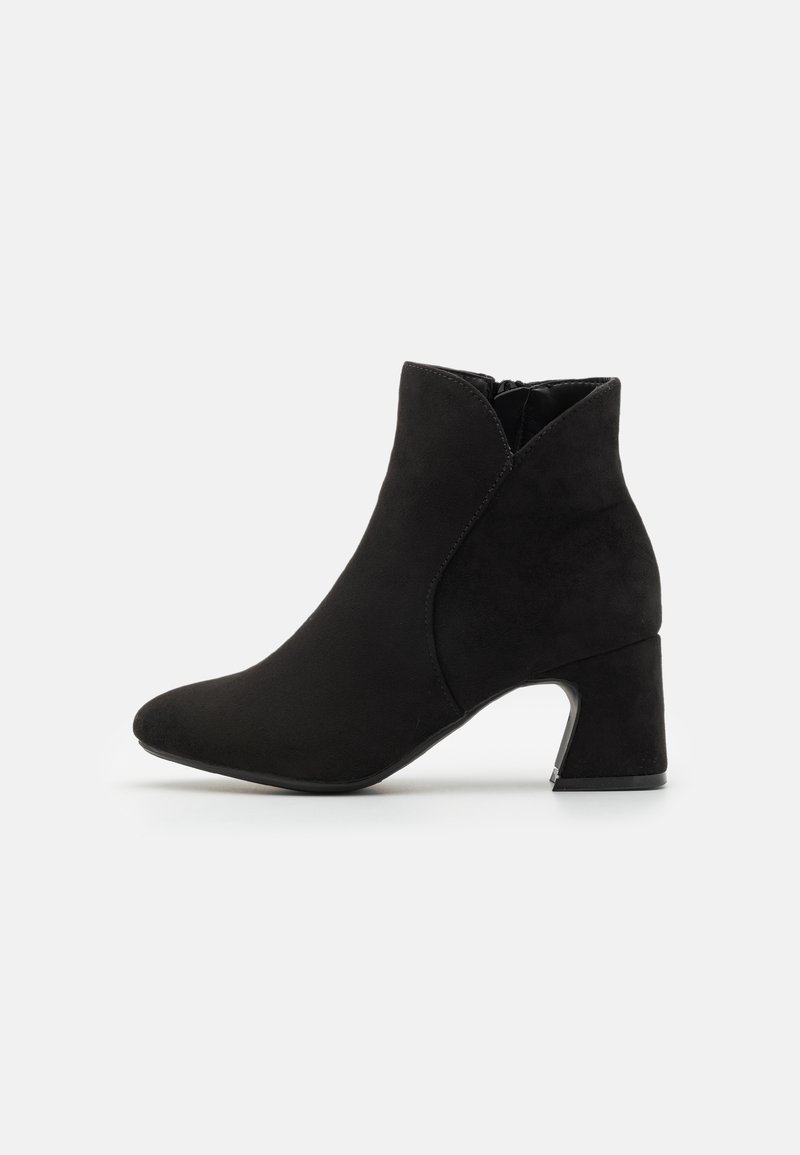 Botas de tobillo de ante negro con punta afilada, recortes laterales y un tacón medio en bloque. Presentan una textura suave y un diseño minimalista.