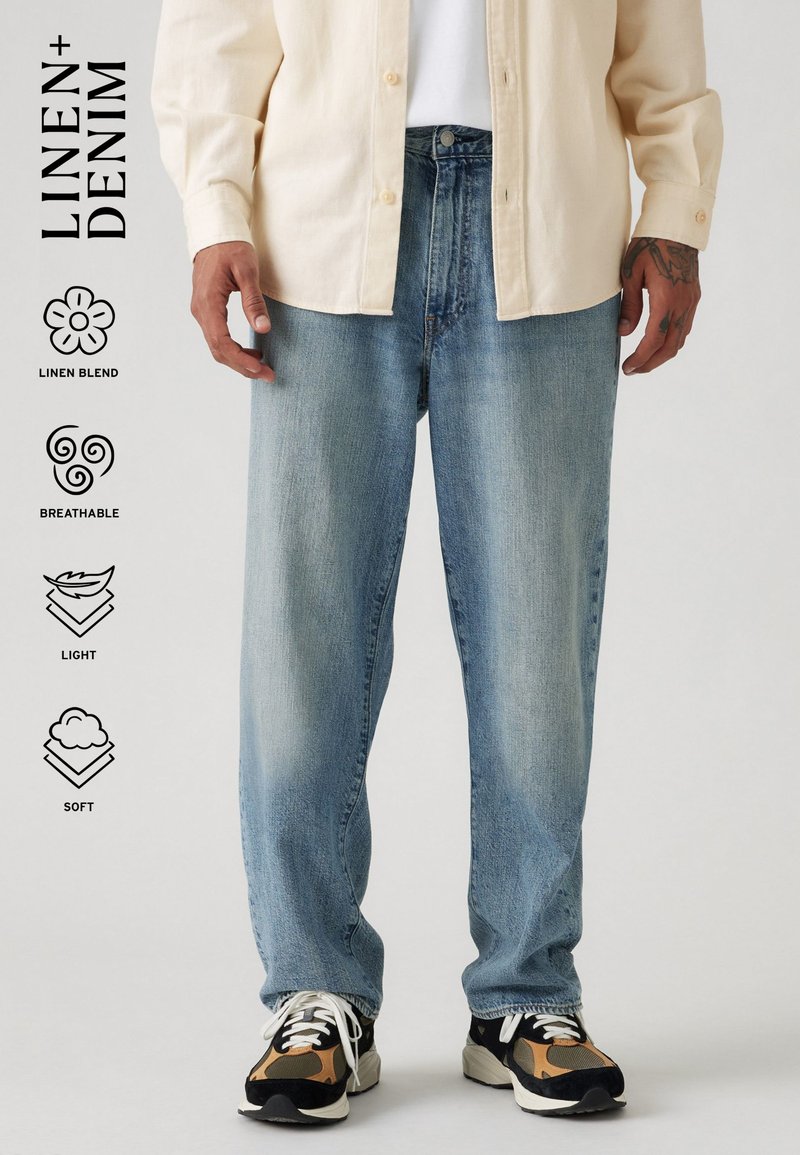Lichtblauwe linnenmix jeans met een losse pasvorm, zachte textuur en vervaagd ontwerp. G gedragen met een crème overhemd met knopen en zwarte sneakers.
