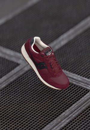 Maroon sneaker crafted from suede and mesh, featuring a black accent, white sole, rounded toe, and textured surface with visible laces.