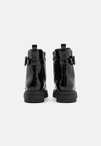 Bottines en cuir verni noir avec une semelle en caoutchouc épaisse, accents de boucle subtils et une languette à l'arrière pour un enfilage facile.