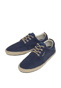 Zapatillas de lona en navy con cordones beige, suelas de goma y un acento de cuerda de yute alrededor de la base. Presentan el logo en el lateral y un diseño de punta redonda.
