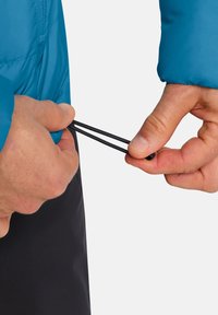 Blaue isolierte Jacke mit glatter Textur, die einen schwarzen Kordelzug hat, der angezogen wird. Nahaufnahme von Händen, die die Passform anpassen.