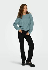 Pull en tricot bleu clair avec des manches oversized, associé à un jean noir à jambe droite et des mocassins à semelle épaisse noirs.