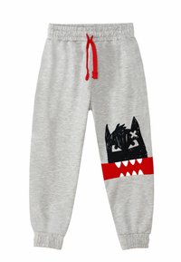 Graue Sweatpants mit elastischem Bund und rotem Kordelzug. Mit einem schwarzen Monster-Graphic und roten Akzenten am Unterschenkel sowie weißen Zähnen.