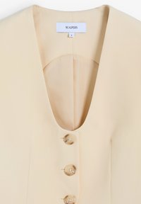 Chaleco sin mangas beige con escote profundo en V, tres grandes botones a juego en la parte frontal y etiqueta de la marca "Scalpers" talla pequeña en el interior del cuello.