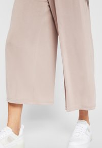 Pantalones cortos de color beige claro, hechos de una tela suave, con una cinturilla elástica y dobladillo cosido. Combinados con zapatillas blancas.