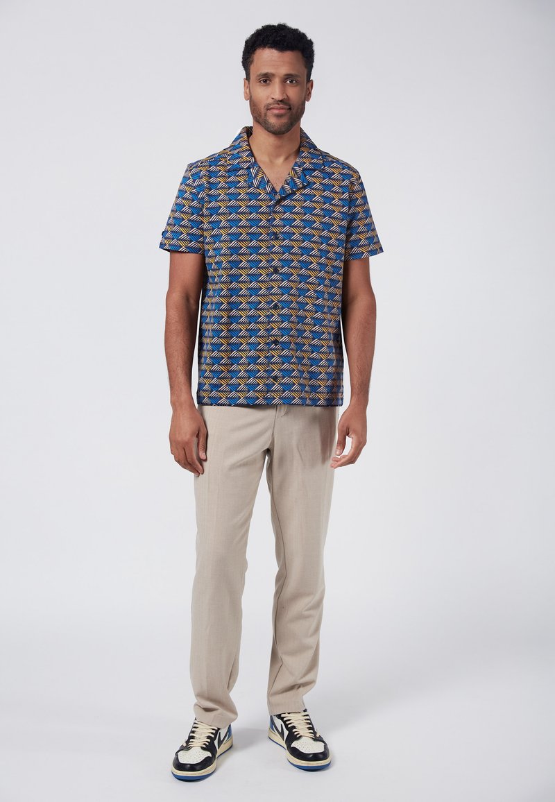 Camisa de botones de manga corta con un patrón geométrico en azul y naranja, combinada con pantalones beige y zapatillas negras con acentos blancos.