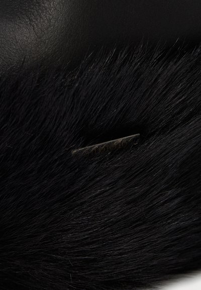 Black faux fur fabric with a small dark metal tag partially visible, engraved with "STUDIO ID" lettering.