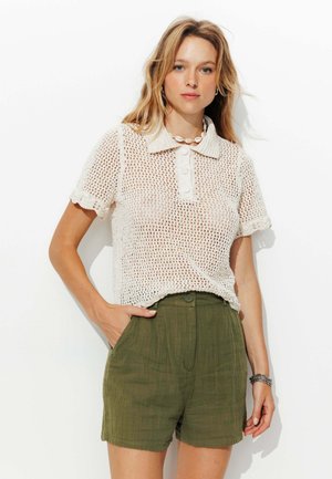 Polo en maille de couleur crème clair avec col et patte de boutonnage ; associé à un short texturé vert olive avec poches latérales.