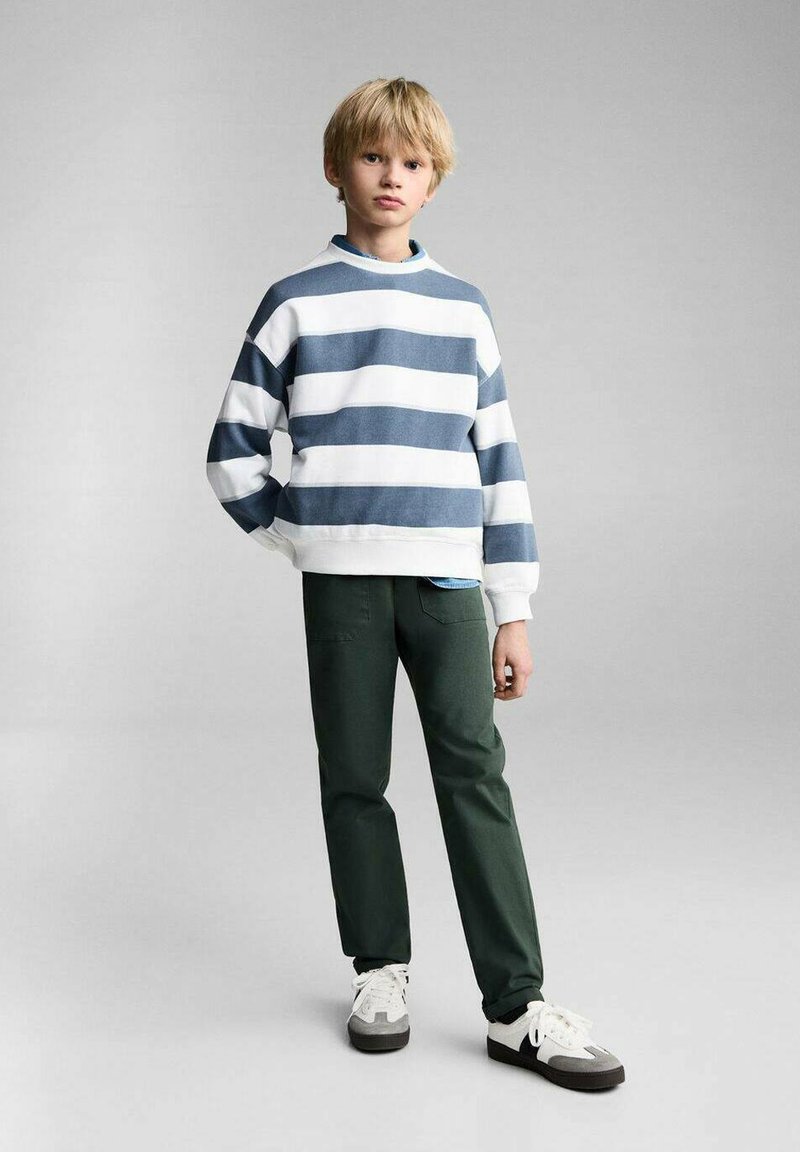 Felpa a righe blu e bianche, pantaloni verdi e sneakers. La felpa ha un collo rotondo e una vestibilità fluida; i pantaloni sono attillati con tasche.