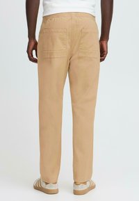 Beige chinos med elastisk midjebånd, to baklommer og avslappet passform, kombinert med beige og hvite sneakers.