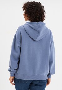 Felpa blu con una vestibilità rilassata, cappuccio grande e polsini a coste. Il tessuto appare morbido, con una superficie liscia e senza motivi visibili.