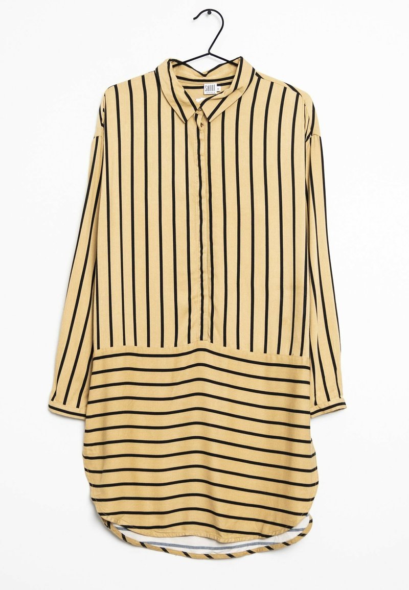 Robe chemise beige à manches longues avec des rayures verticales noires sur le haut et des rayures horizontales sur la partie inférieure, suspendue sur un cintre noir.