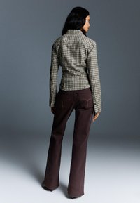 Zielono-beżowa, w kratę dopasowana marynarka z długimi rękawami, połączona z ciemnobrązowymi spodniami dzwonami, widziana z tyłu na szarym tle.