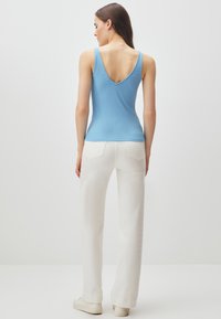 Canotta a coste color azzurro chiaro con scollatura a V, abbinata a pantaloni bianchi a gamba larga, dotati di tasche posteriori e tessuto strutturato.