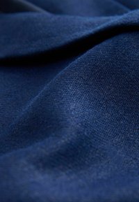 Pehme, tumesinist kangast peene kudumistruktuuriga, kergelt kortsus, rõhutamas materjali detaili ja värvi sügavust.