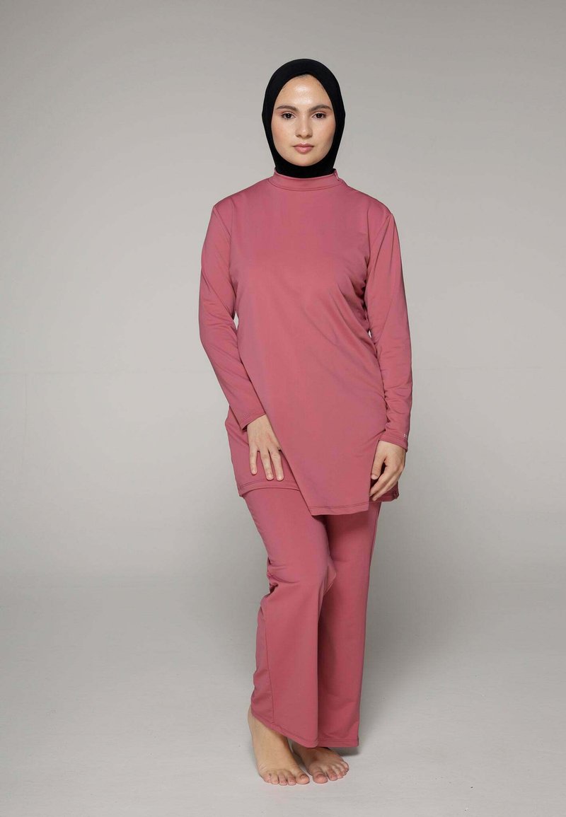 Roze tuniek met lange mouwen en bijpassende brede broek van een zachte stof. Het heeft een hoge hals en zijsplitten voor bewegingsgemak.