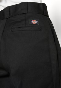 Black work pants made of durable fabric, featuring a back pocket with a rectangular Dickies logo patch. Clean lines and a tailored fit.