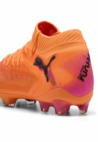 Scarpe da calcio Puma arancioni e rosa con logo Puma nero, lacci e tacchetti progettati per il gioco su terreno solido.