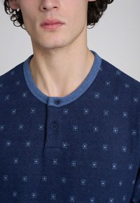 Maglietta henley blu navy con un motivo testurizzato, colletto azzurro a contrasto e due bottoni sullo scollo.
