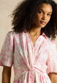 Ziedu raksta kleita gaiši rozā un baltā krāsā, ar īsām pūkainām piedurknēm, mezgla vidukļa detaļu un apkakles dekoltē, izgatavota no mīksta auduma.