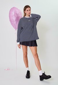 Tengerészkék és fehér csíkos, hosszú ujjú ing, amelyet egy pliszírozott fekete szoknyával párosítottak. Fekete platform cipők; rózsaszín szív alakú léggömb a háttérben.