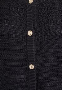 Svart stickad cardigan med ett strukturerat mönster, försett med guldknappar fram. Tyget är mjukt med en ribbad kant.