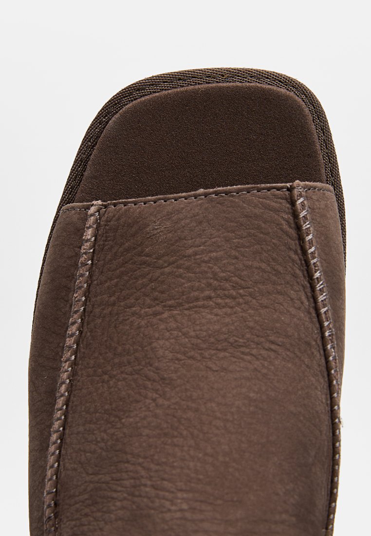 Zapatilla de cuero marrón con una superficie texturizada, punta redonda y detalles de costura en los laterales. Forro suave en la abertura para mayor comodidad.