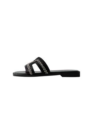 Chanclas negras con dos correas recortadas decoradas con un patrón tejido. Suela plana con una textura suave.