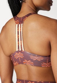 BH med brun bunn, dekorert med et oransje palmetre-mønster. Racerback-design med kremfargede vertikale striper og teksturert materiale.