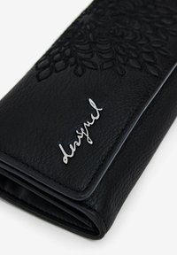 Mustapintainen nahkalompakko, jossa on kohoava kukkakuosi, hopeinen "Desigual"-logo ja teksturoitu pinta. Taitettuna elegantin modernissa muodossa.