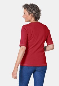 Rotes kurzärmliges Hemd mit runder Ausschnitt und kontrastierenden Nähten, kombiniert mit blauen Jeans, die eine lockere Passform und glatte Textur zeigen.