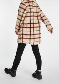 Ruteret fleecejakke i creme, rød og sort; hætte-design; parret med sorte leggings og sorte vandresko med strukturerede såler.