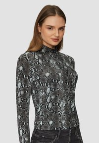 Haut à manches longues en imprimé serpent noir et gris. Col haut, design ajusté, texture lisse. Associé à un pantalon noir avec des embellissements.