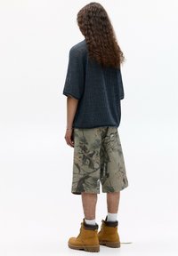 Top din bumbac cu mânecă scurtă, de culoare bleumarin, asortat cu șorturi camuflate până la genunchi și cizme bej cu un accent maro, prezentând un model de țesătură texturată.