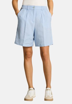 Person wearing light blue knee-length shorts with pockets, paired with white and beige sneakers, standing against a plain background.