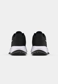 Zapatos deportivos negros con un upper texturizado, que cuentan con una entresuela blanca y una suela de goma con patrón. Acentos plateados en el talón.