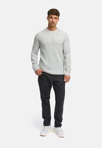 Pullover a coste grigio chiaro con scollatura a girocollo, abbinato a jeans scuri e sneakers bianche con dettagli grigi e suola spessa.