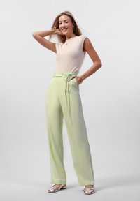 Lichtroze geribbelde mouwloze top gecombineerd met hoogwater, mintgroene wijde broek met een strikceintuur. Zilveren platte schoenen.