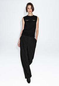 Black sleeveless top with two front pockets and silver accents, paired with black, wide-leg pants. Smooth texture and minimalist design.