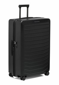 Valigia rigida nera con design scanalato, chiusura a zip singola, manico retrattile e quattro ruote per la mobilità.