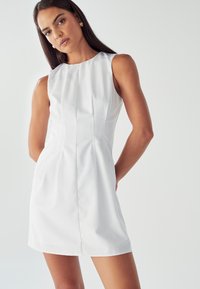 Biele bezrukávové šaty s kulatým výstrihom, s vertikálnymi švami a priliehavým strihom, vyrobené z hladkej látky.