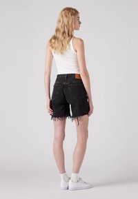 Black denim shorts with frayed hems, high waist, and rear pocket details. Paired with a white tank top and white sneakers.