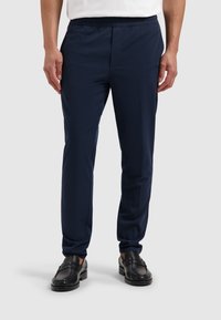 Marineblauwe sportbroek met een elastische tailleband, taps toelopende pasvorm en een gladde textuur. Vergezel je met zwarte instapschoenen voor een casual uitstraling.