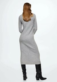Robe grise en tricot avec manches longues, col haut et silhouette moulante ; portée avec des bottes en cuir noir montant jusqu'aux genoux.
