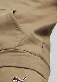 Felpa beige con tasca a marsupio, tessuto morbido e logo Puma bianco sul davanti. Presenta un piccolo etichetta nera con dettagli.