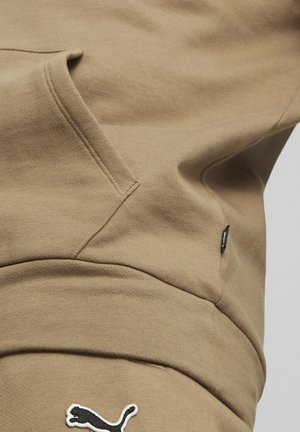 Felpa beige con tasca a marsupio, tessuto morbido e logo Puma bianco sul davanti. Presenta un piccolo etichetta nera con dettagli.